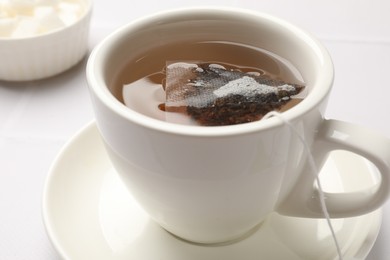 Tea bag in cup with hot drink on white table, closeup