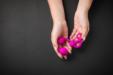 Young woman holding pink anal balls on black background, top view with space for text. Sex toy