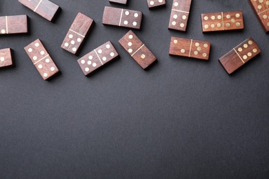 Photo of Wooden domino tiles on black background, flat lay. Space for text