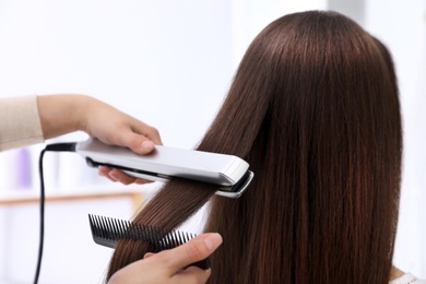 Photo of Hairdresser using modern flat iron to style client's hair in salon