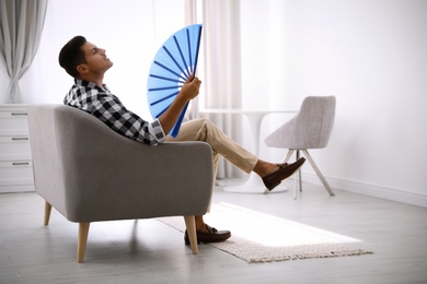 Photo of Man with hand fan sitting on sofa. Summer season