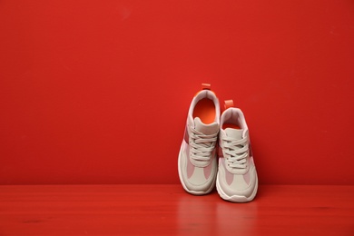 Stylish women's sneakers on wooden table near red wall, space for text