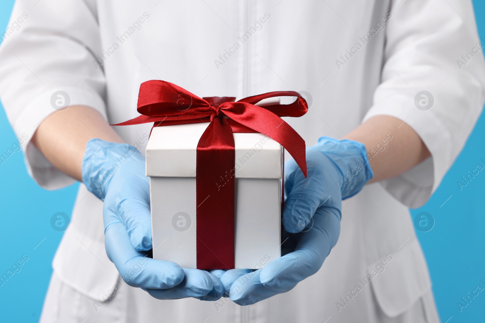 Photo of Doctor holding gift box on light blue background, closeup. Medical present