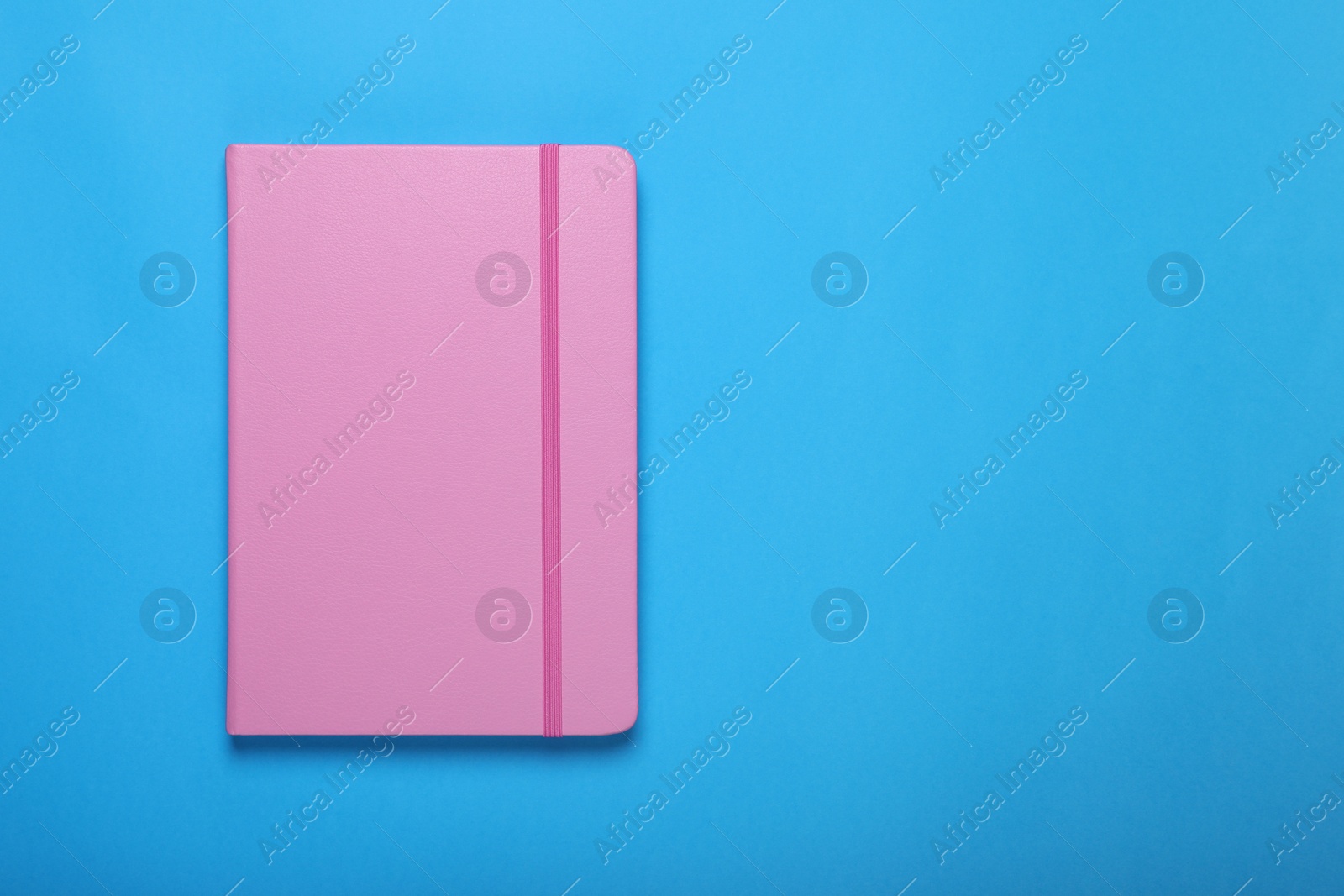 Photo of Pink notebook on light blue background, top view. Space for text