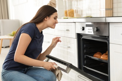 Photo of Beautiful woman opening door of oven with baked buns in kitchen
