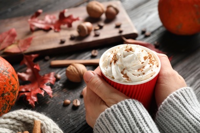 Woman holding paper cup with tasty pumpkin spice latte at black wooden table, closeup