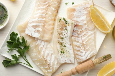 Photo of Fresh raw cod fillets with spices and lemon on white wooden table, flat lay