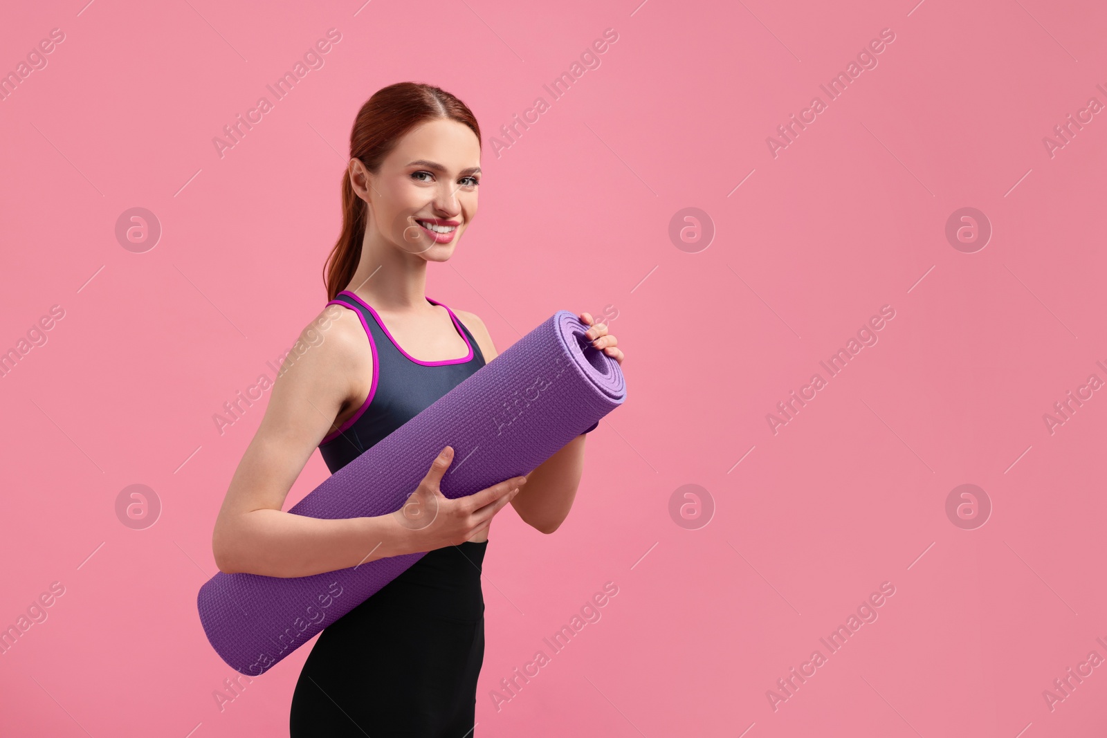 Photo of Woman in sportswear with fitness mat on pink background, space for text