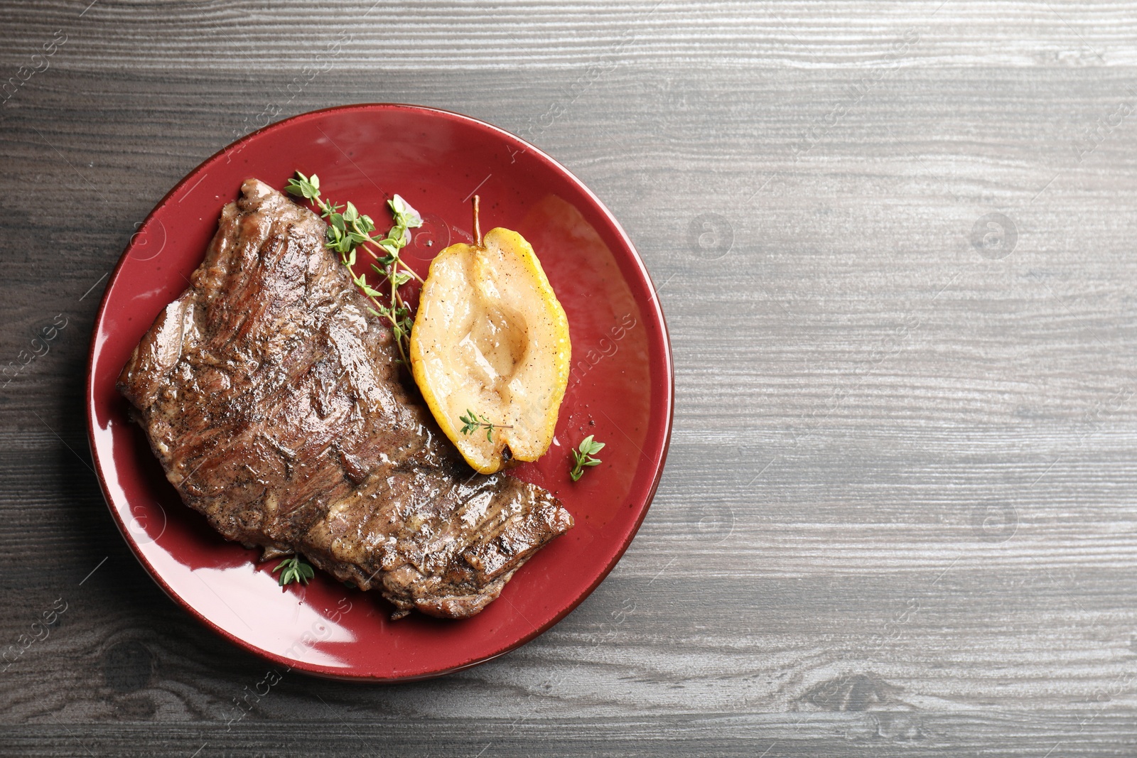 Photo of Delicious roasted beef meat, caramelized pear and thyme on grey wooden table, top view. Space for text