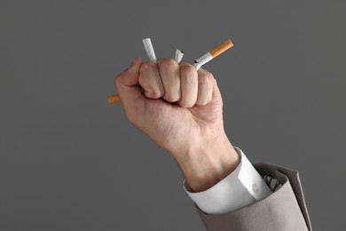 Photo of Stop smoking concept. Man crushing cigarettes on gray background, closeup