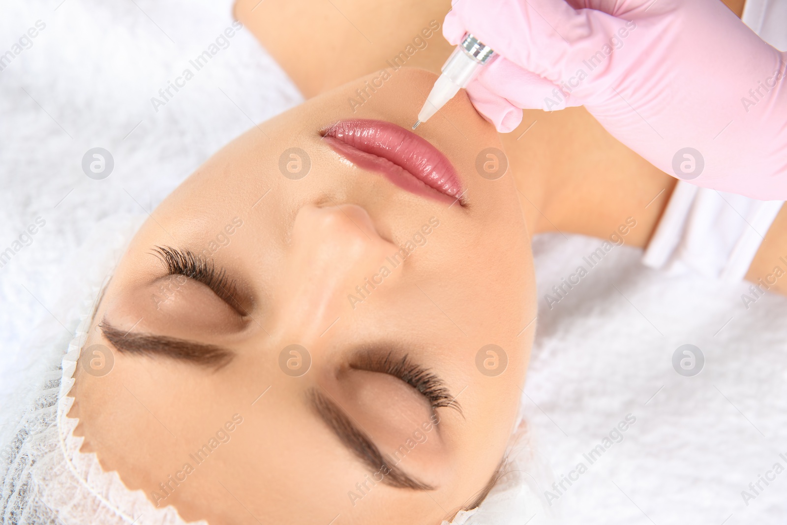 Photo of Young woman getting permanent makeup on lips in beautician salon, closeup