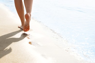 Photo of Woman walking on sandy seashore, closeup of legs