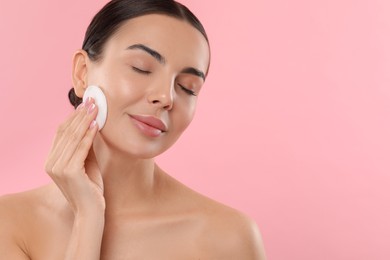 Photo of Beautiful woman removing makeup with cotton pad on pink background. Space for text