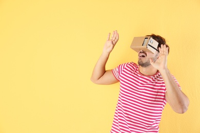 Photo of Young man using cardboard virtual reality headset on color background. Space for text