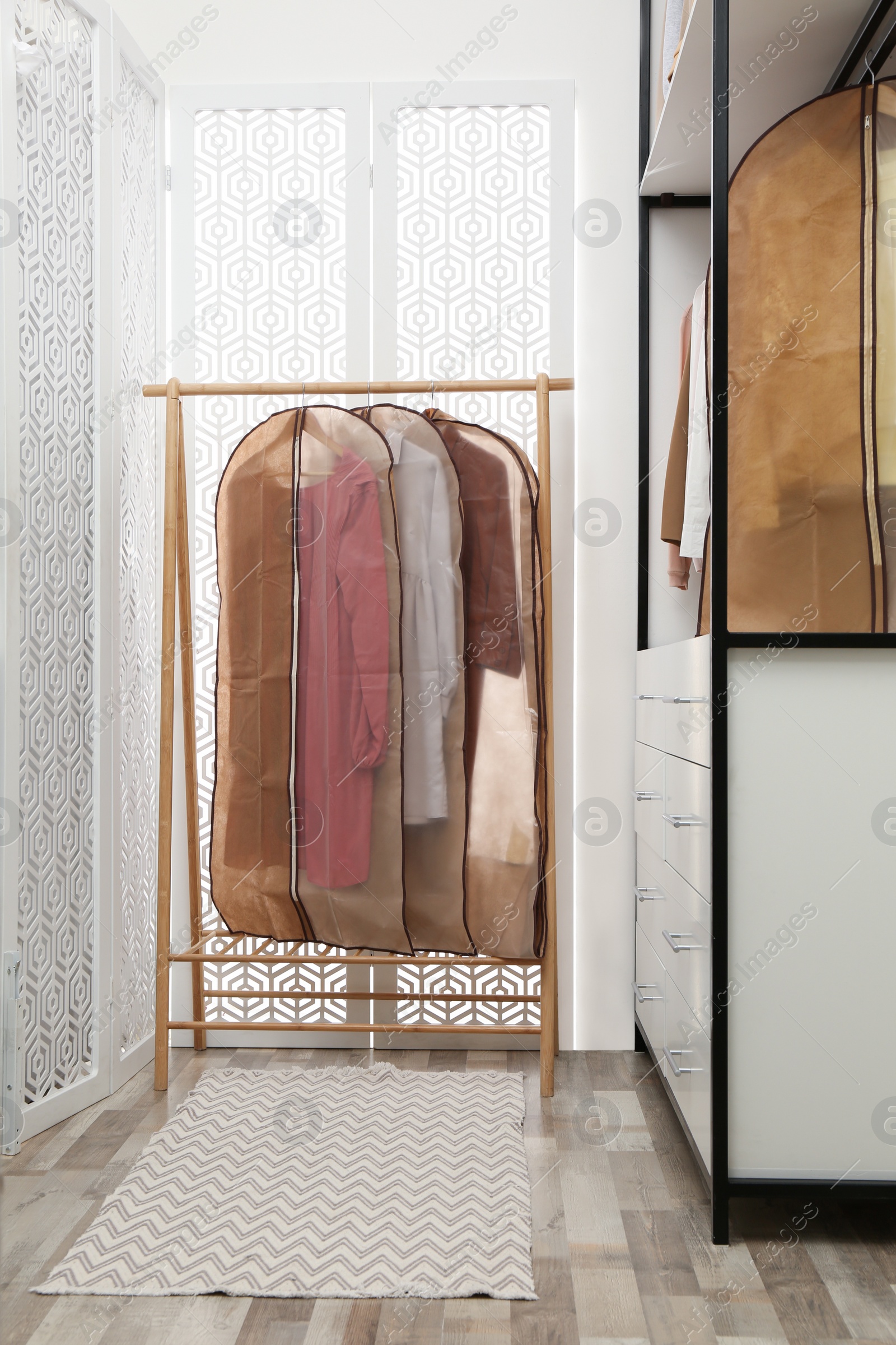 Photo of Garment bags with clothes on rack in dressing room