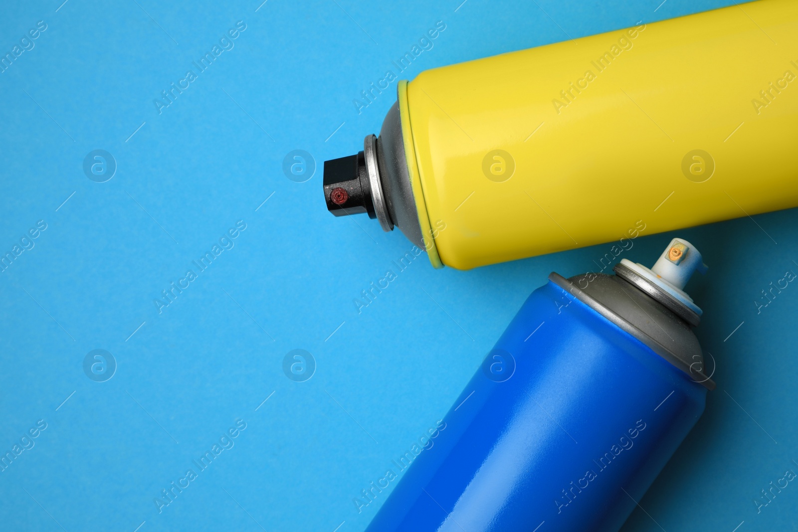 Photo of Cans of different graffiti spray paints on light blue background, flat lay. Space for text