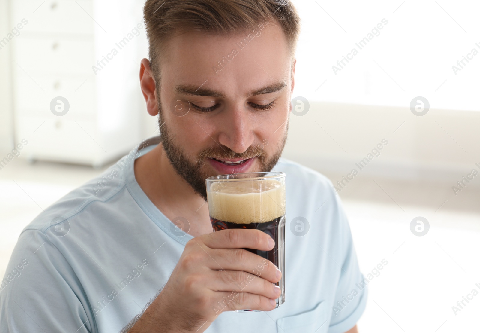 Photo of Handsome man with cold kvass indoors. Traditional Russian summer drink