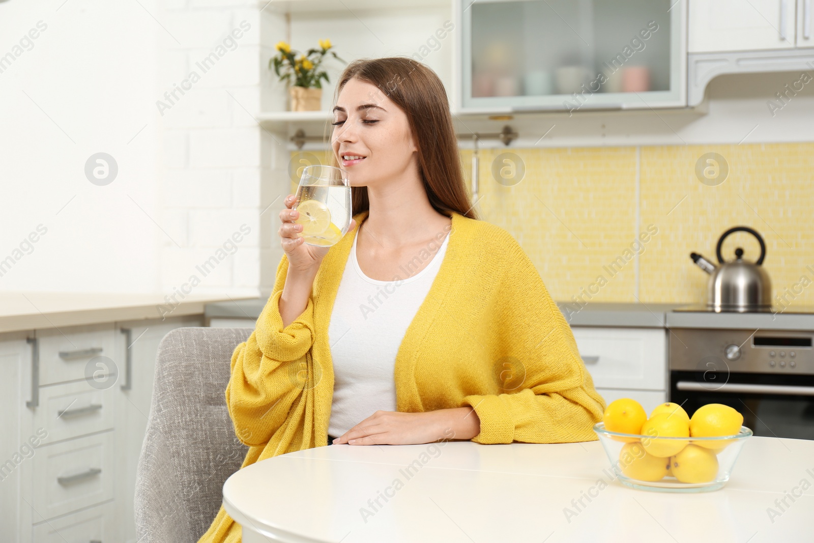 Photo of Young woman drinking lemon water in kitchen