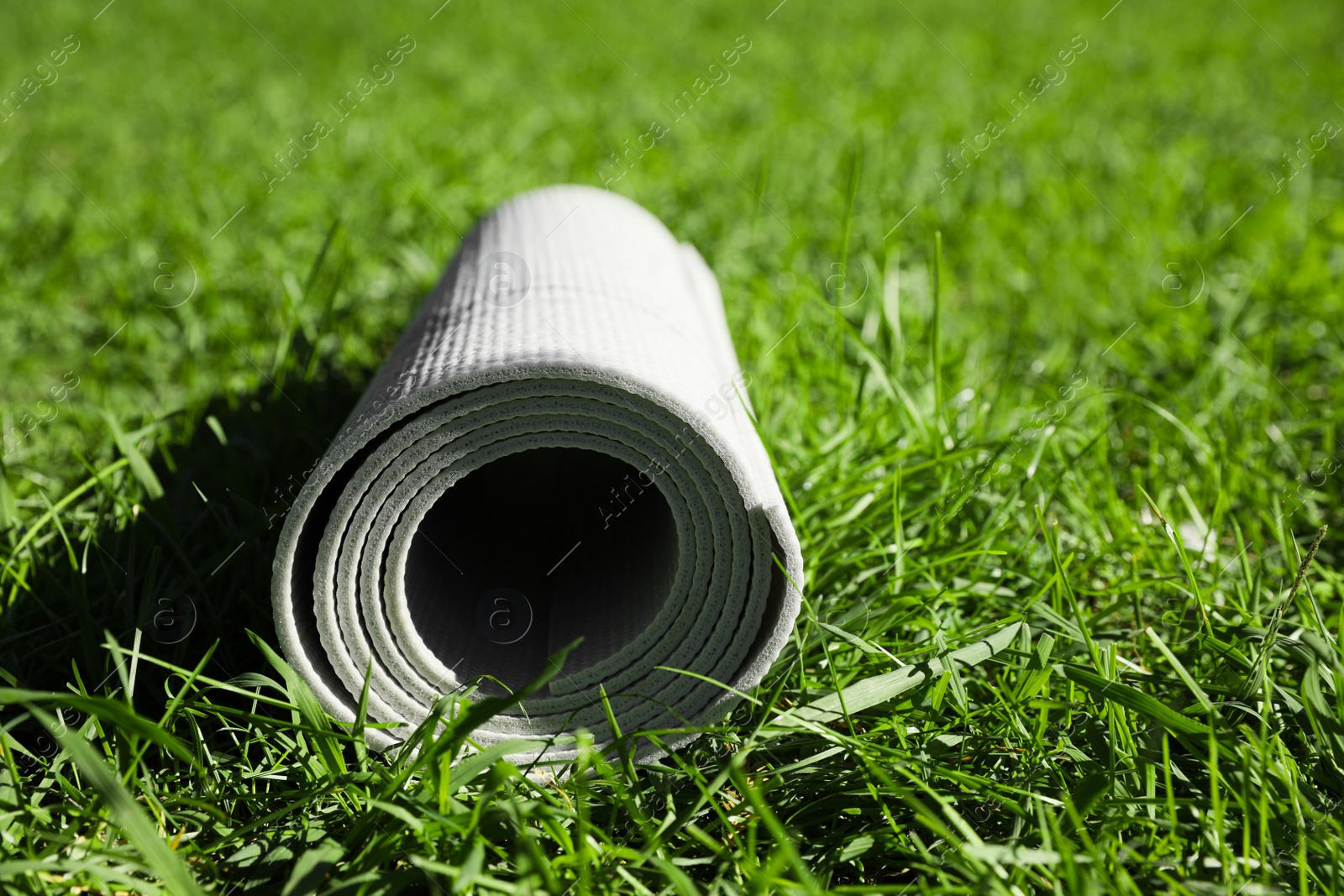 Photo of Rolled karemat or fitness mat on green grass outdoors, closeup. Space for text