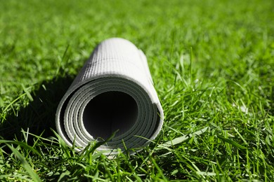 Rolled karemat or fitness mat on green grass outdoors, closeup. Space for text