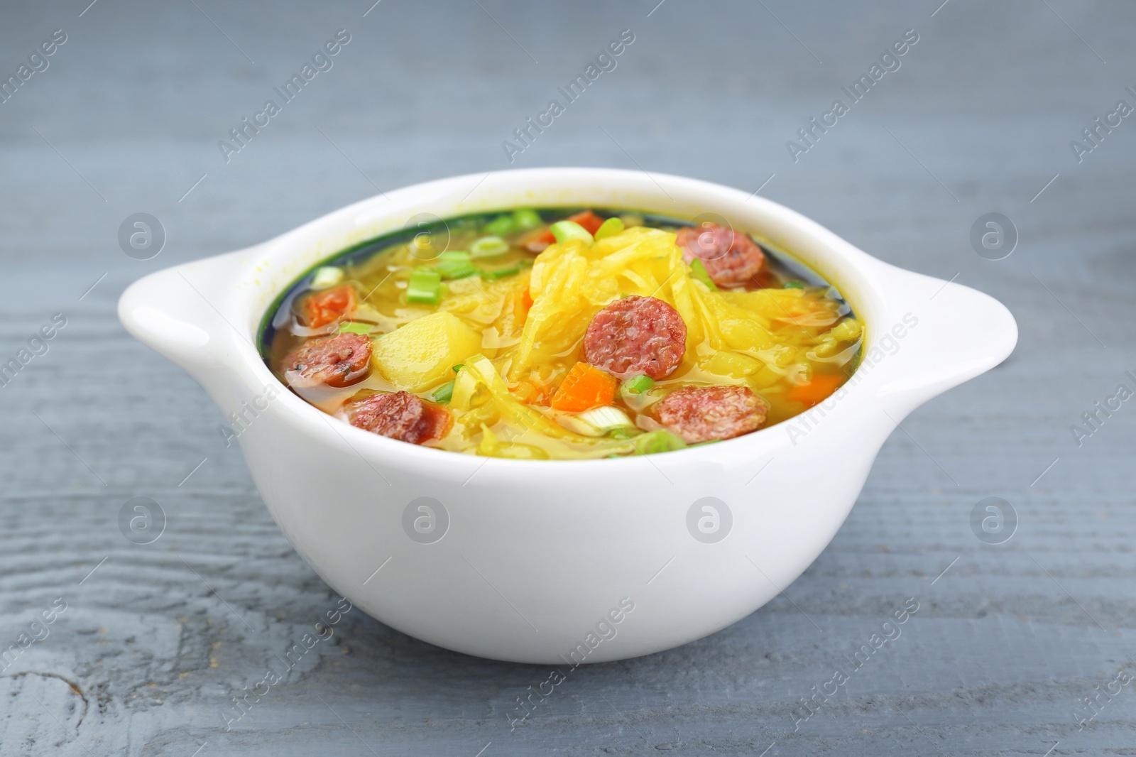 Photo of Delicious sauerkraut soup with smoked sausages and green onion on grey wooden table