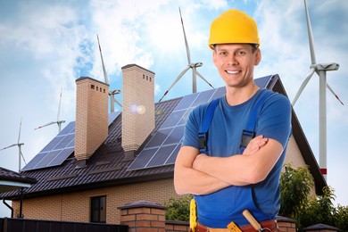 Worker with tool belt and view of wind energy turbines near house with installed solar panels on roof