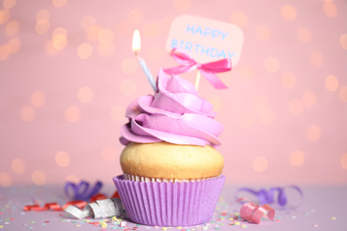 Beautiful birthday cupcake, streamers and confetti against pink background with blurred lights