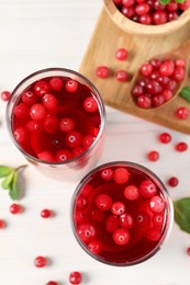 Photo of Tasty cranberry juice in glasses and fresh berries on white wooden table, flat lay