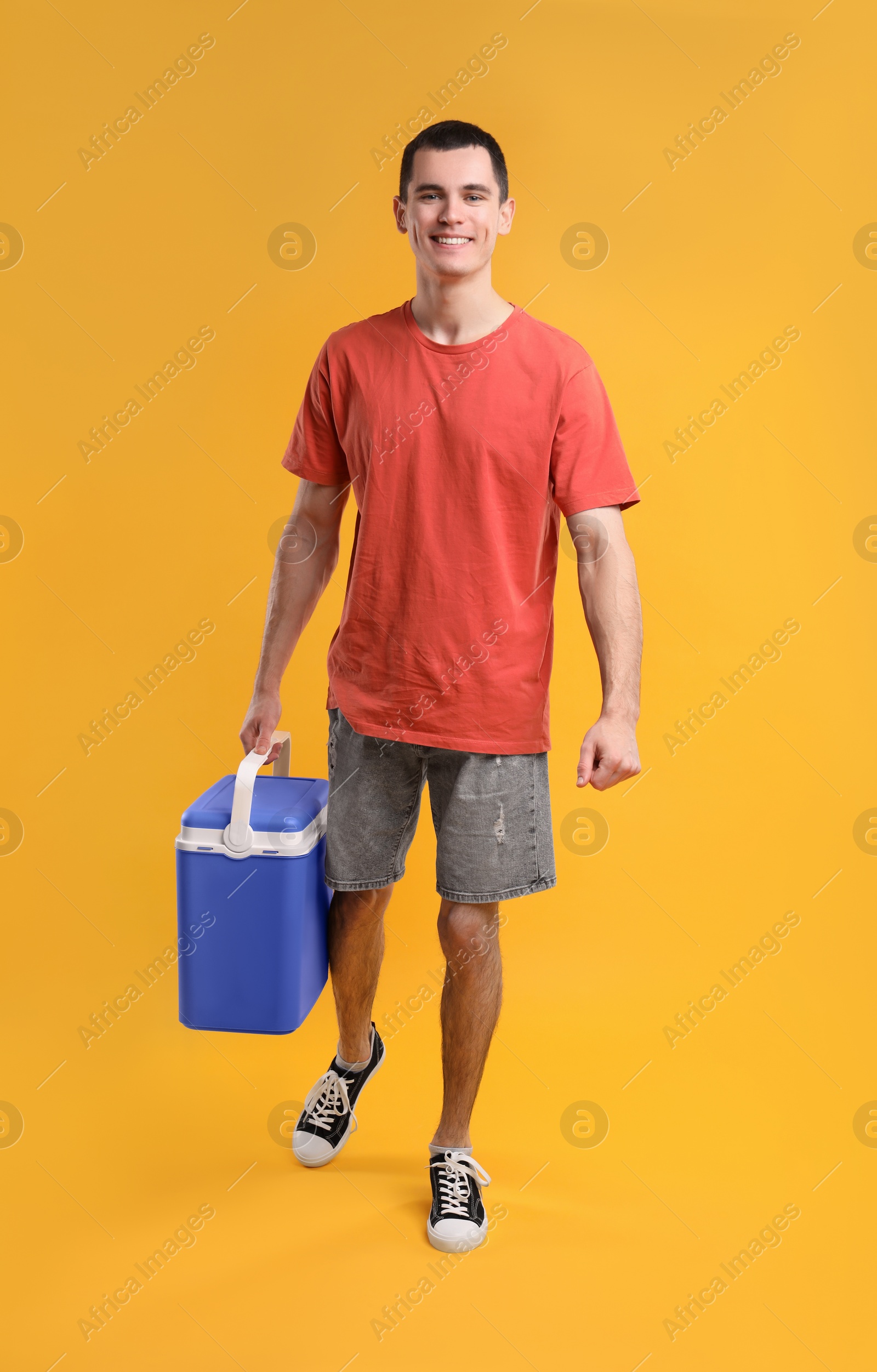 Photo of Man with blue cool box walking on orange background