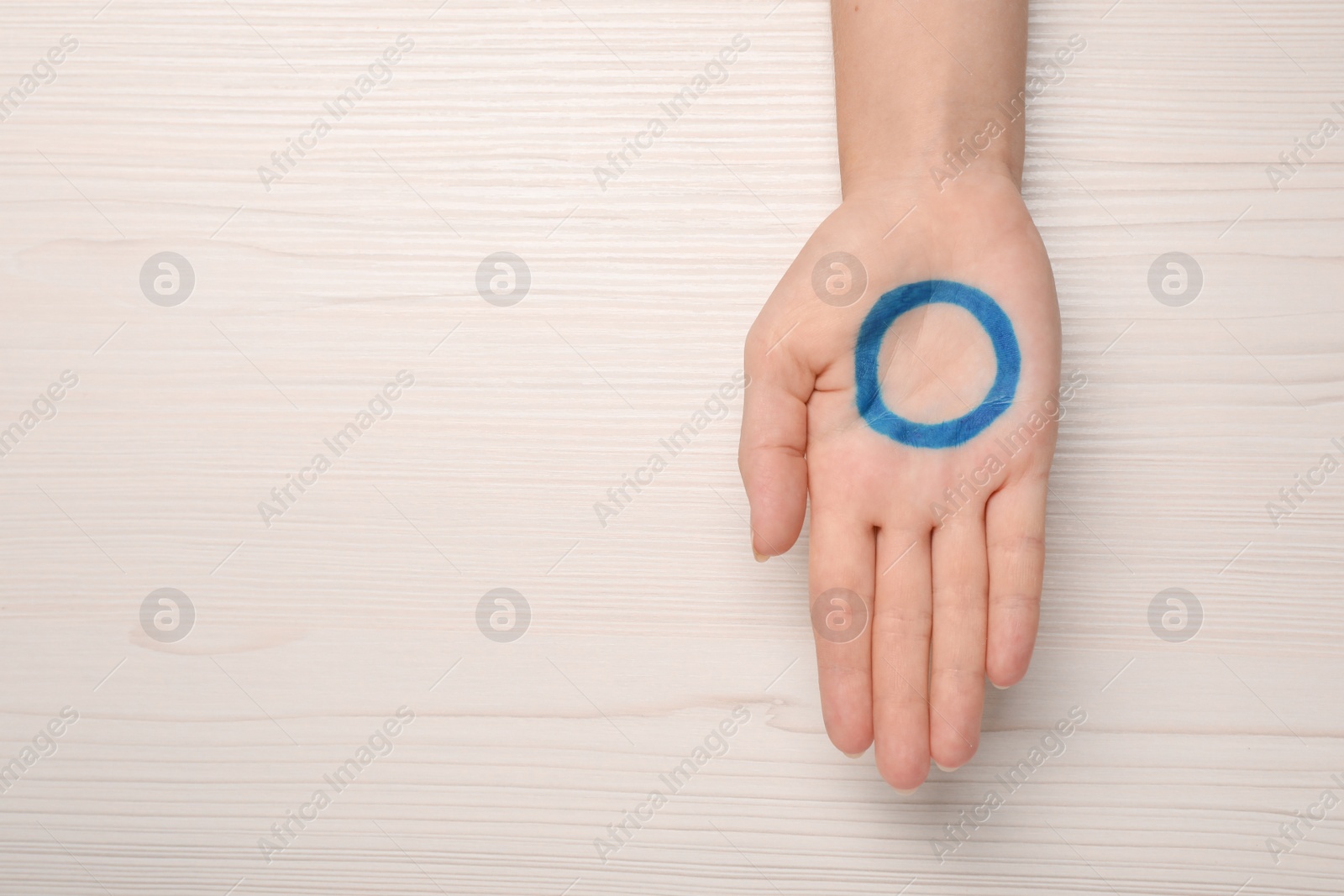 Photo of Woman showing blue circle as World Diabetes Day symbol at white wooden table, top view with space for text