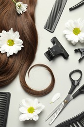 Photo of Flat lay composition with professional hairdresser tools, flowers and brown hair strand on light grey background