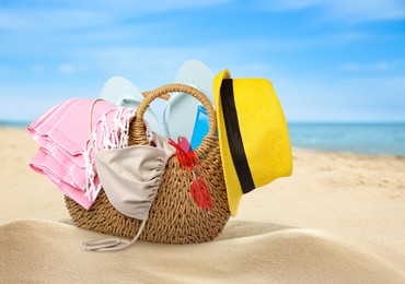 Image of Stylish bag with different accessories on sandy beach near ocean