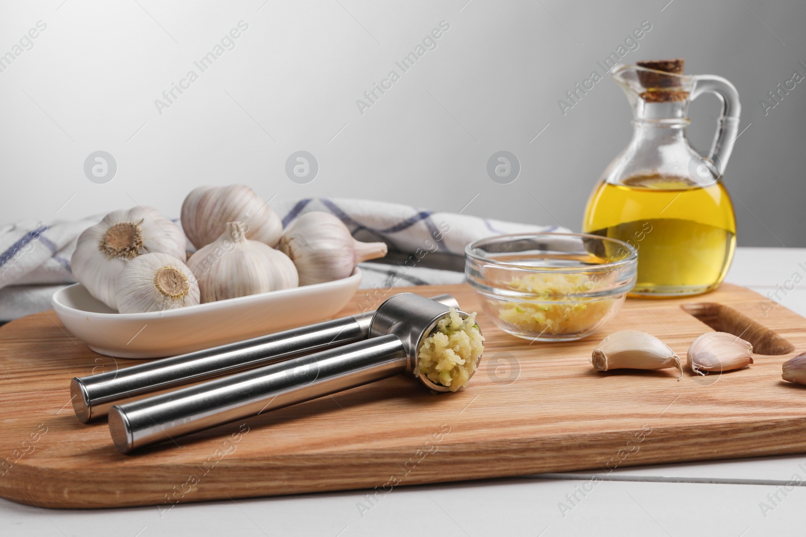 Photo of One metal press and crushed garlic on white wooden table