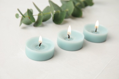 Photo of Burning light blue candles and eucalyptus branch on light table