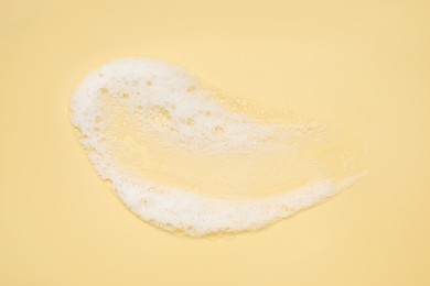 Smudge of white washing foam on yellow background, top view