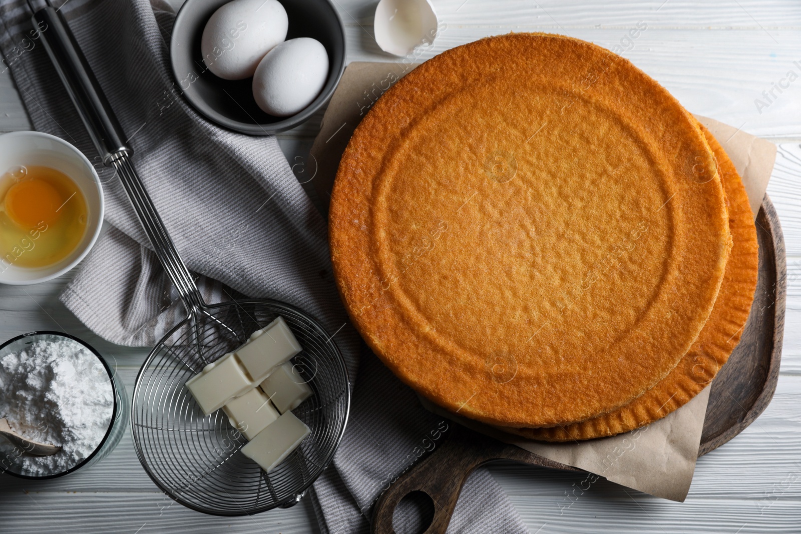 Photo of Delicious homemade sponge cake and ingredients on white wooden table, flat lay