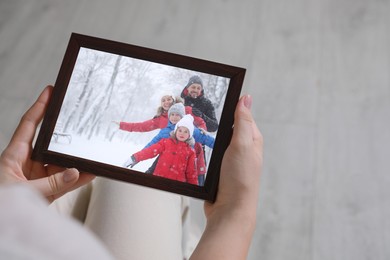 Image of Woman holding frame with photo portrait of her family indoors, closeup