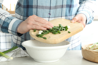 Photo of Woman putting chopped green spring onion into bowl on table, closeup