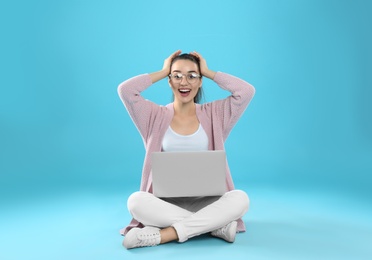 Surprised young woman in casual outfit with laptop sitting on color background