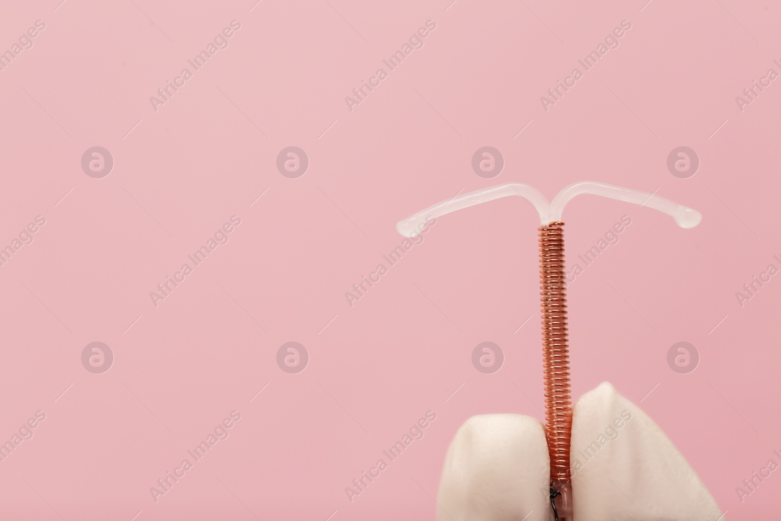 Photo of Doctor holding T-shaped intrauterine birth control device on pink background, closeup. Space for text