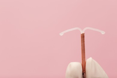 Photo of Doctor holding T-shaped intrauterine birth control device on pink background, closeup. Space for text