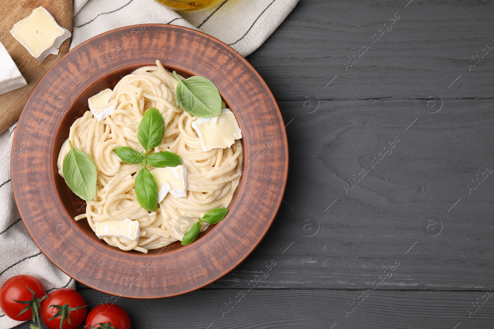 Photo of Delicious pasta with brie cheese, basil leaves and tomatoes on grey wooden table, flat lay. Space for text