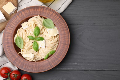 Delicious pasta with brie cheese, basil leaves and tomatoes on grey wooden table, flat lay. Space for text