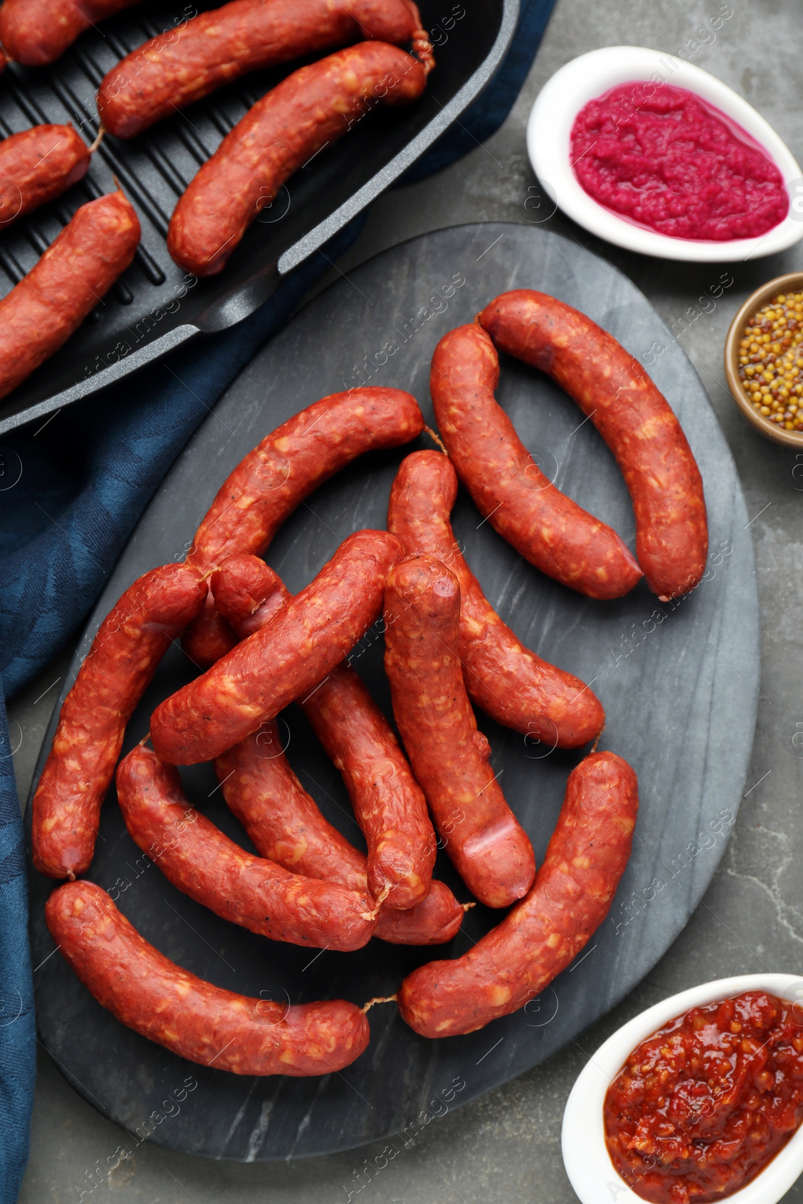 Photo of Delicious sausages, ketchup, mustard and horseradish on grey table, flat lay