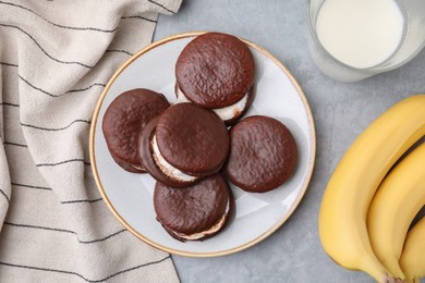 Photo of Tasty sweet choco pies, bananas and glass of milk on light gray table, flat lay