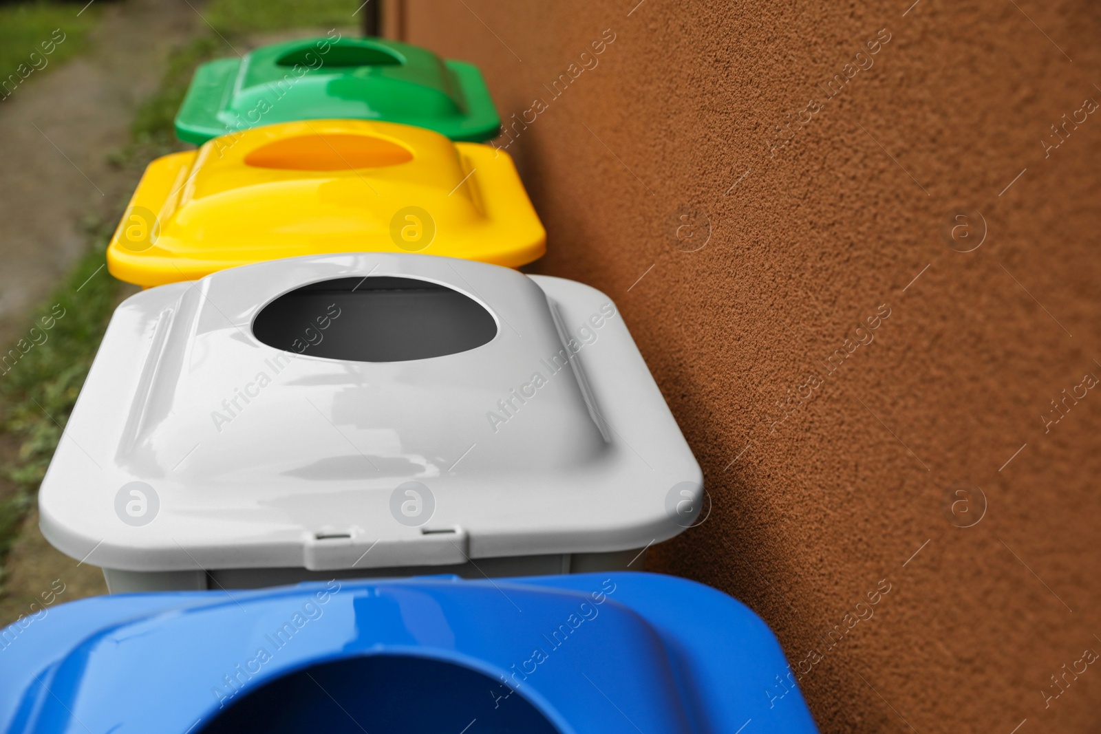 Photo of Many color recycling bins near brown wall outdoors, closeup