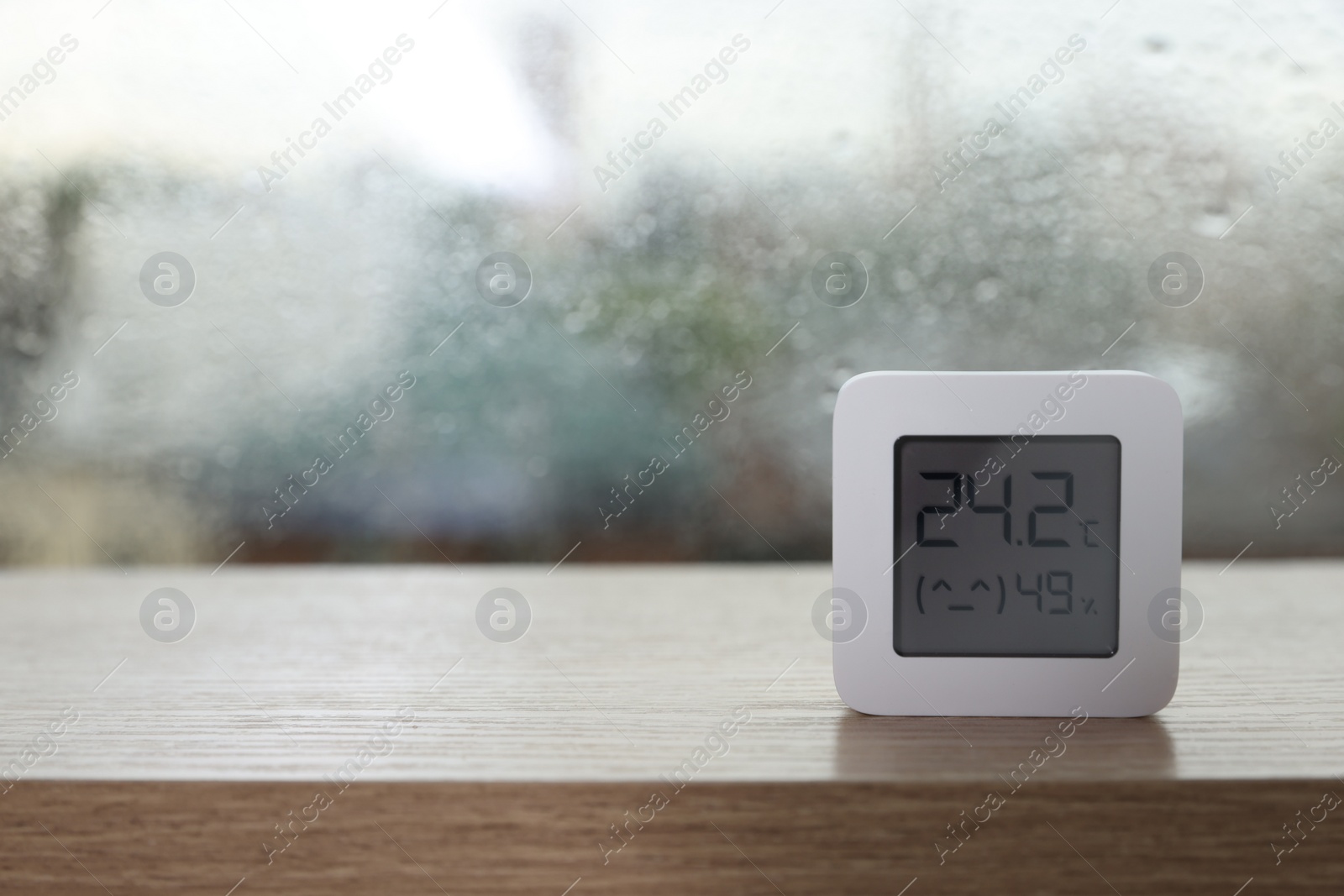 Photo of Digital hygrometer with thermometer near window on rainy day. Space for text