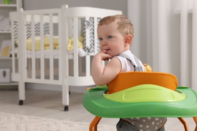 Portrait of cute baby with toy walker at home, space for text. Learning to walk
