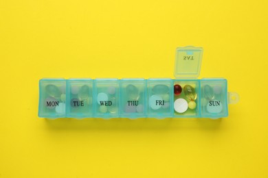 Photo of Plastic box with different pills on yellow background, top view