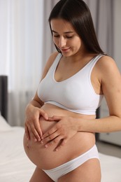 Photo of Beautiful pregnant woman in stylish comfortable underwear making heart with hands on her belly indoors